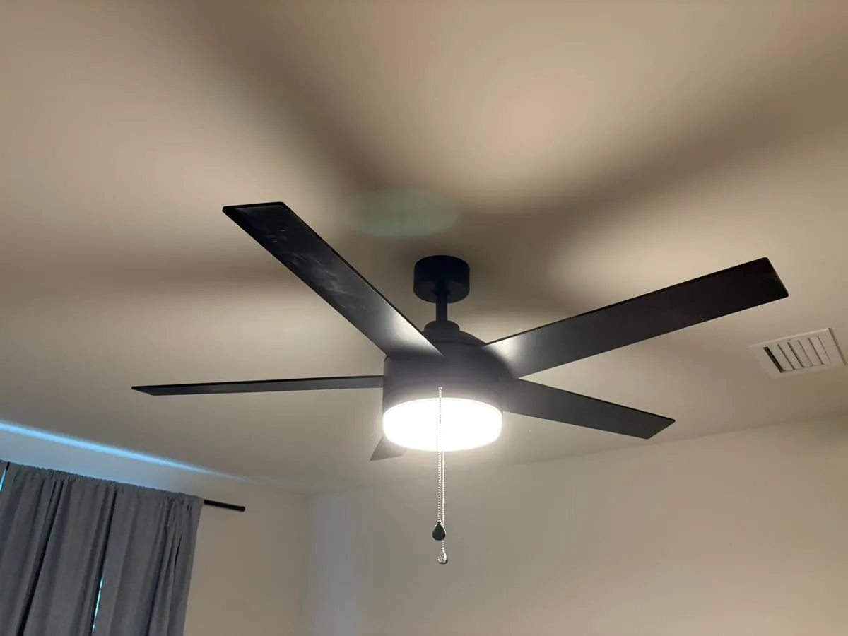 New black five-blade ceiling fan with integrated LED light, installed and running in a bedroom