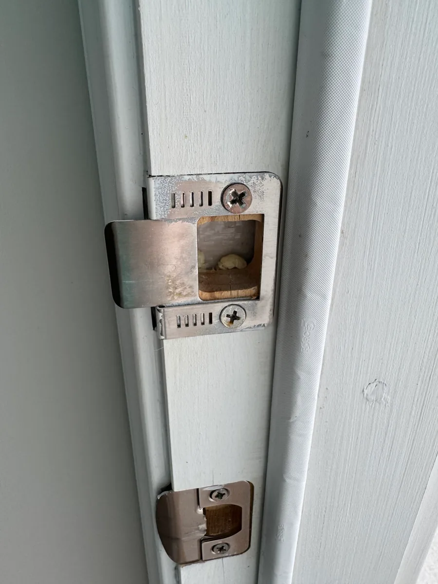 A door jamb with the deadbolt strike plate refitted and its tab adjusted, and the latch strike below it.