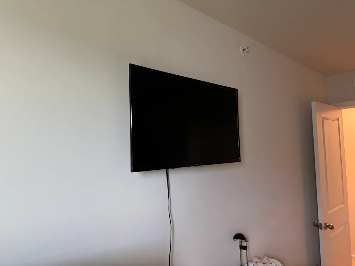 A small TV wall-mounted high on a guest bedroom wall, positioned to clear a computer desk below it.